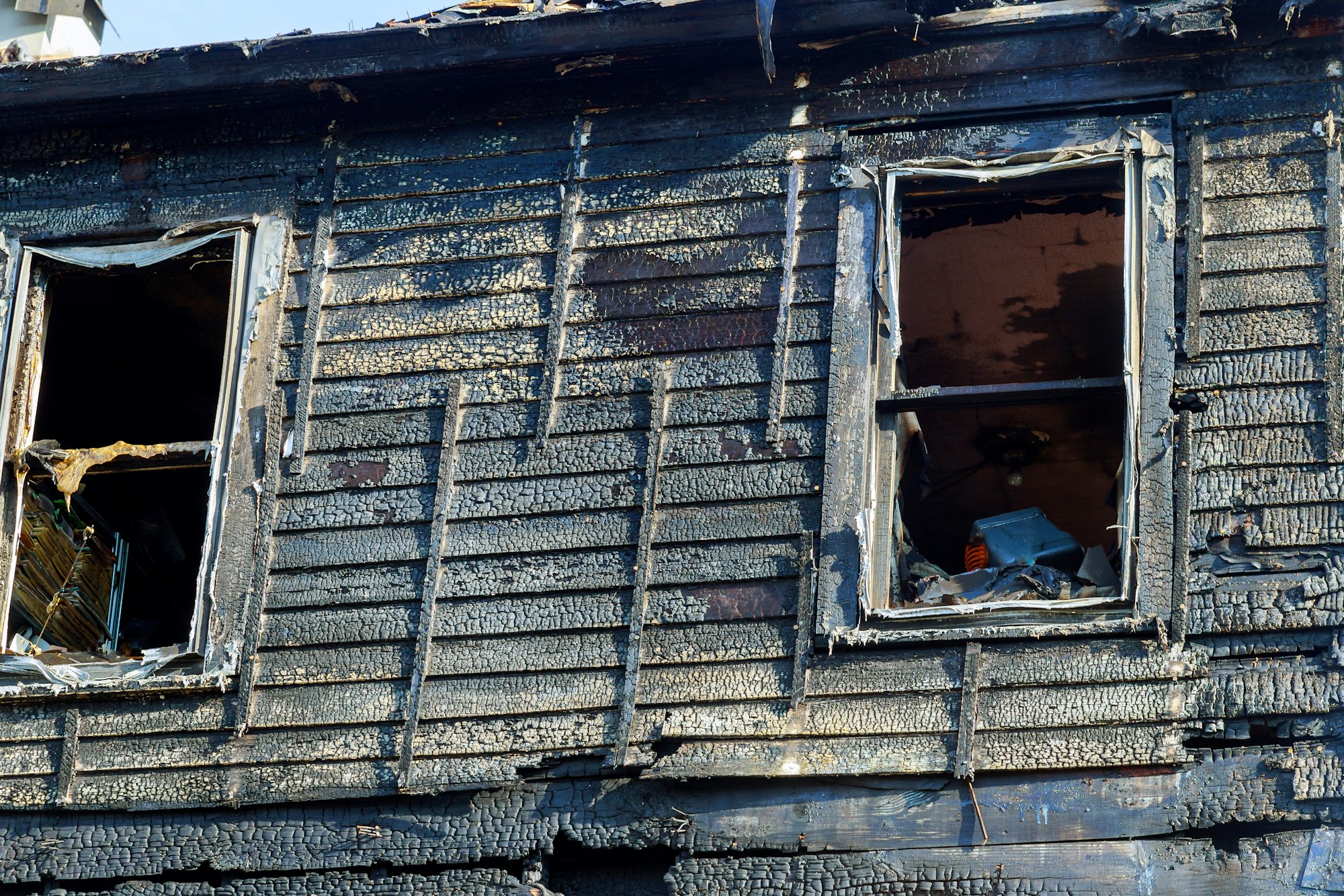 Burnt black house after fire line in front of a destroyed home.